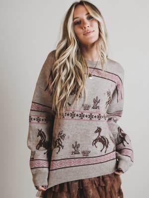 Woman wearing a patterned sweater with horse designs on a plain background