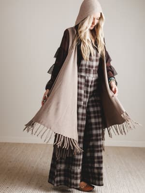 Person wearing a plaid jumpsuit with a brown hooded vest indoors.