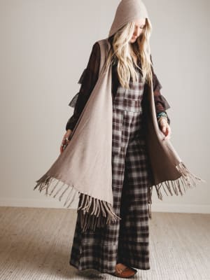 Person wearing a plaid outfit with a brown coat and scarf indoors.