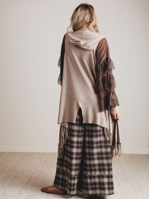 Person wearing a layered outfit with a plaid skirt and shawl against a plain background