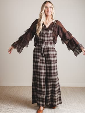 Woman wearing a plaid jumpsuit with a brown blouse against a plain background