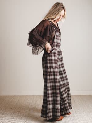 Woman wearing a plaid jumpsuit with sheer sleeves against a plain background