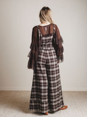 Person wearing a plaid dress with a brown shawl over shoulders against a plain background