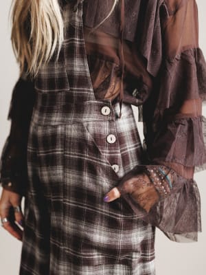 Person wearing a plaid dress with brown jacket and gloves on a plain background