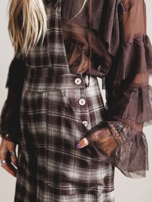 Person wearing a plaid dress with brown jacket and gloves on a plain background