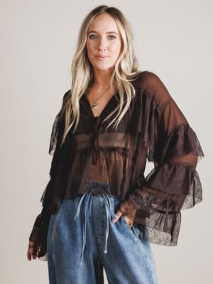 Woman wearing a sheer brown blouse with long sleeves and blue jeans against a plain background