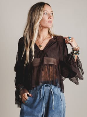 Woman wearing a brown blouse with sheer sleeves and blue jeans against a plain background