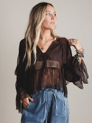 Woman wearing a brown blouse with sheer sleeves and blue jeans against a plain background