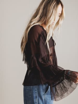 Woman wearing a dark brown blouse with lace details and blue jeans on a plain background