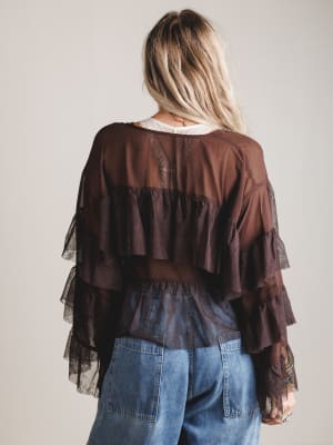 Person wearing a brown layered blouse and blue jeans against a plain background