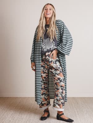 Woman wearing a long striped coat over a patterned outfit on a plain background