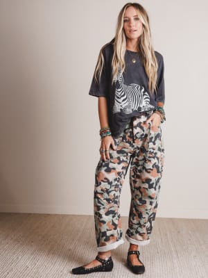 Woman wearing a graphic t-shirt and camouflage pants indoors.