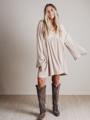Woman wearing a beige dress and brown cowboy boots against a plain background