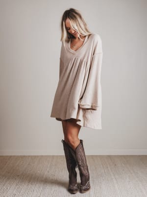 Woman wearing a beige dress and brown boots against a plain background