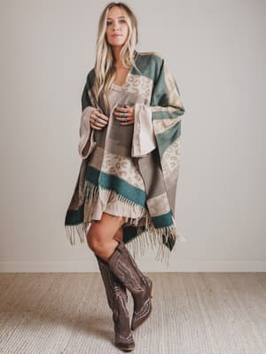 Woman wearing a patterned shawl and brown boots in a neutral setting
