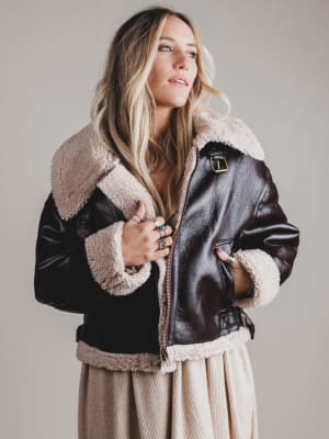 Woman wearing a black leather jacket with beige fur lining against a plain background