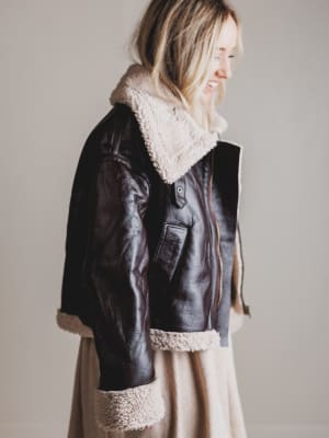 Person wearing a black leather jacket with shearling collar and cuffs on a plain background