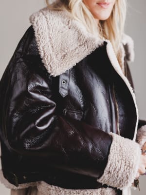 Close-up of a black leather jacket with beige fur lining on a neutral background