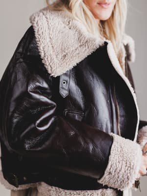 Close-up of a black leather jacket with beige fur lining on a neutral background