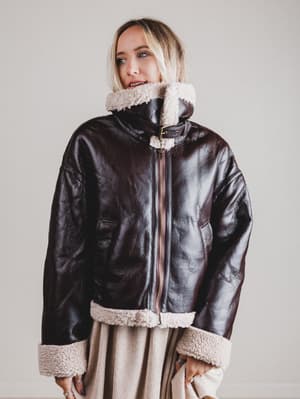 Person wearing a black leather jacket with white fur trim on a plain background