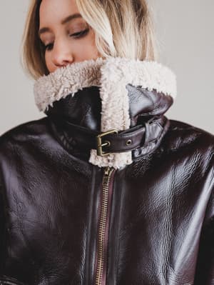 Person wearing a black leather jacket with a shearling collar against a neutral background