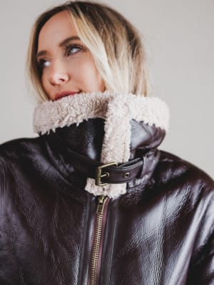 Person wearing a black leather jacket with a fur-lined hood against a neutral background