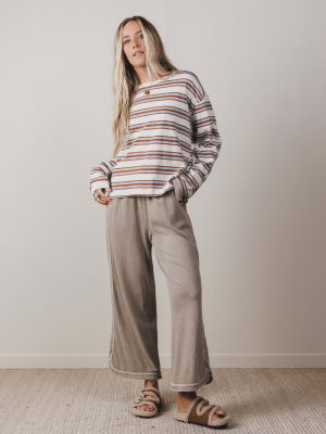 Woman wearing a striped sweater and beige pants against a plain background