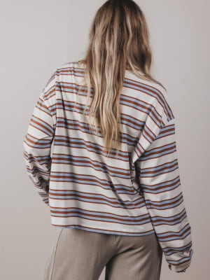 Person wearing a striped shirt with long sleeves and beige pants against a plain background