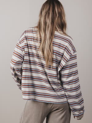 Person wearing a striped shirt with long sleeves and beige pants against a plain background