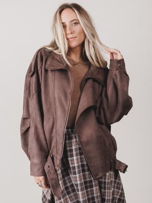Woman wearing a brown jacket over a plaid skirt on a plain background