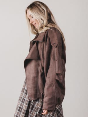 Woman wearing a brown jacket and plaid skirt against a plain background