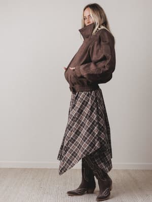 Woman wearing a brown jacket and plaid skirt against a plain background