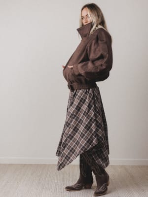 Woman wearing a brown jacket and plaid skirt against a plain background