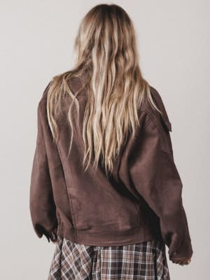 Person wearing a brown jacket and plaid skirt against a plain background