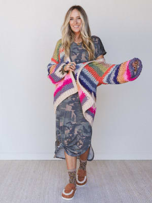 Woman wearing a colorful crochet sweater and holding a matching sock against a white background