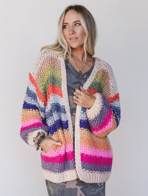 Woman wearing a colorful striped crochet cardigan over a camouflage patterned dress.