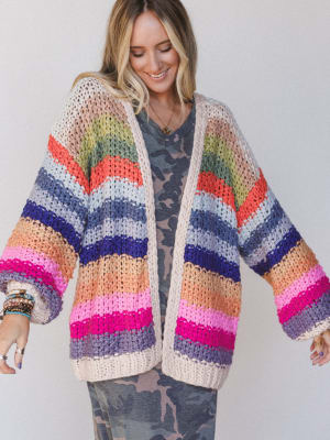 Woman wearing a colorful striped crochet cardigan over a camouflage dress.