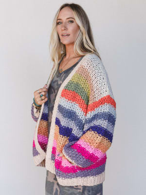 Woman wearing a colorful crocheted cardigan against a plain background