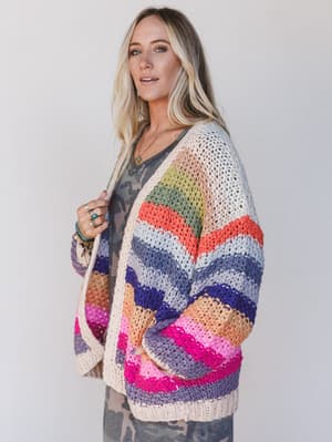 Woman wearing a colorful crocheted cardigan against a plain background