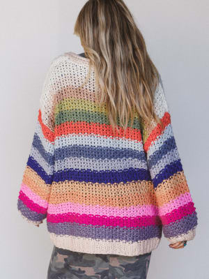 Back view of a woman wearing a colorful striped sweater against a plain background