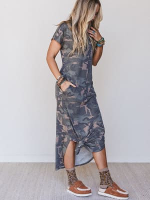 Woman wearing a camouflage dress with patterned socks and sandals on a plain background