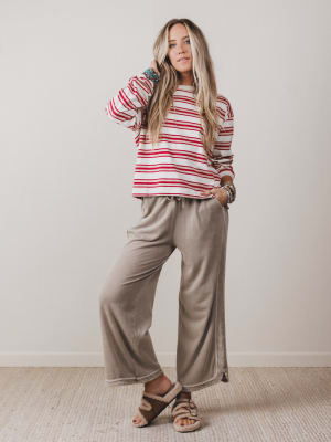 Woman wearing a red and white striped shirt and beige pants against a plain background