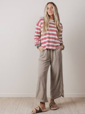 Woman wearing a red and white striped sweater and beige pants against a plain background