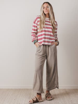 Woman wearing a red and white striped sweater and beige pants against a plain background