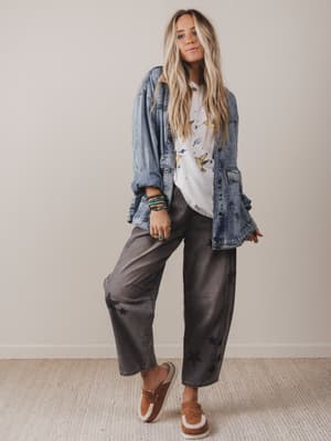 Woman wearing a denim jacket, white shirt, and gray pants against a plain background