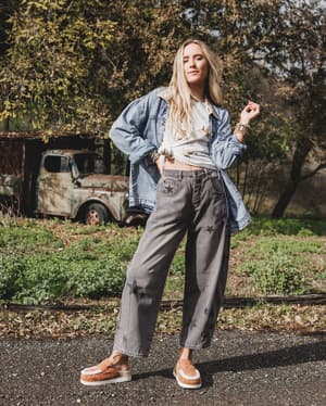 Woman standing outdoors with a rustic background featuring an old truck and trees.