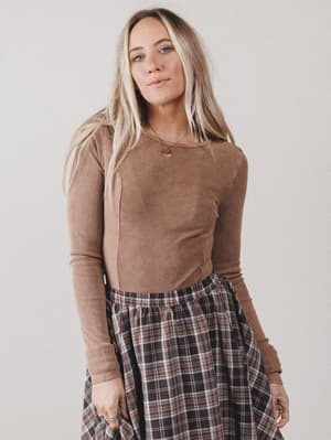 Woman wearing a brown long-sleeve top and plaid skirt against a plain background