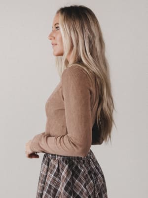 Woman wearing a brown long-sleeve top and plaid skirt against a plain background