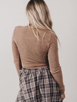 Person wearing a brown long-sleeve top and plaid skirt against a plain background