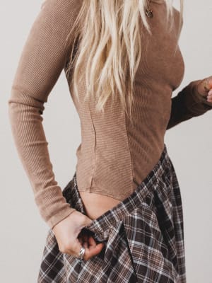 Person wearing a brown ribbed sweater and plaid skirt against a neutral background
